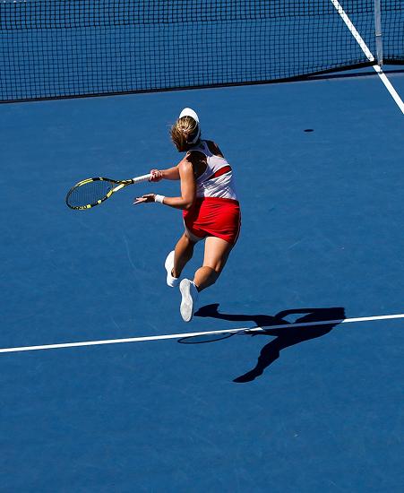 A tennis player wearing red and white is seen mid shot on a blue tennis court